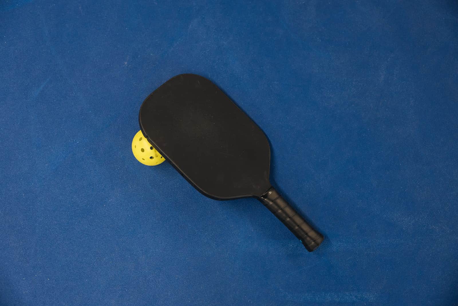A pickleball paddle and ball resting on a blue court surface