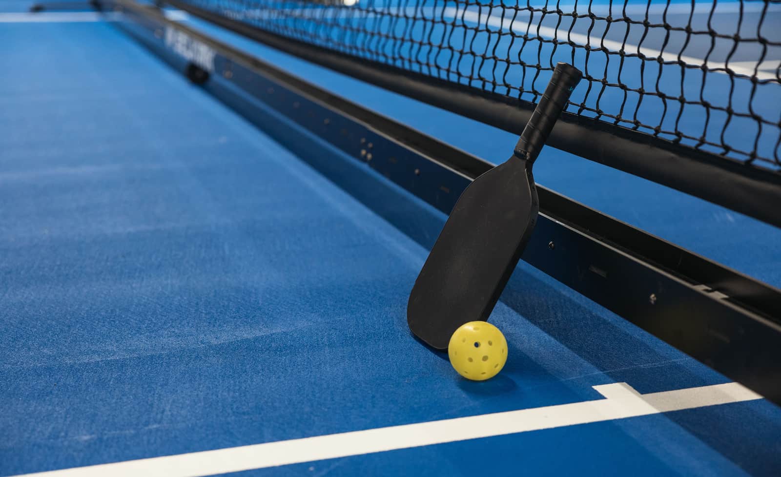 Pickleball paddles and a ball arranged on a light court surface
